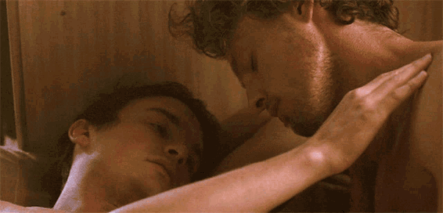 a man and a woman are laying on a bed and kissing
