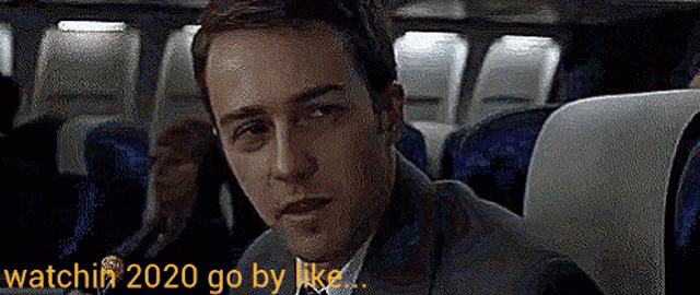 a man sitting on a plane with the words watchin 2020 go by like written below him