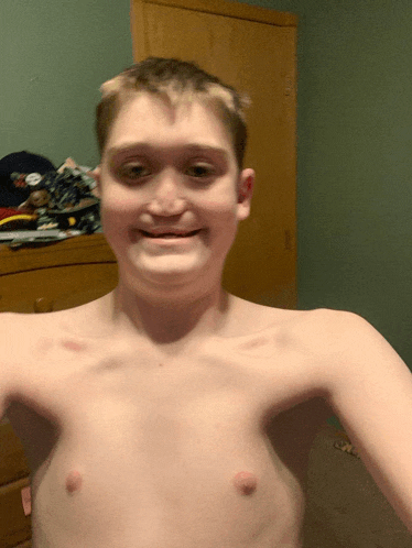 a boy without a shirt is smiling in a room
