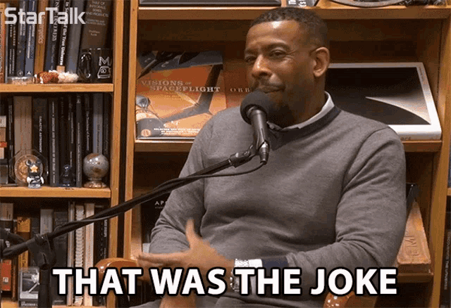 a man sitting in front of a microphone with the words that was the joke written below him