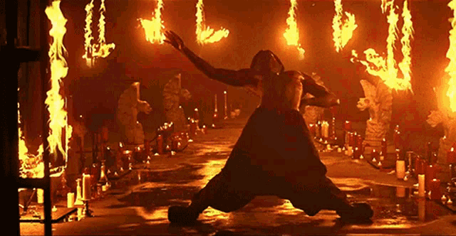 a man is kneeling in front of a wall of flames and candles