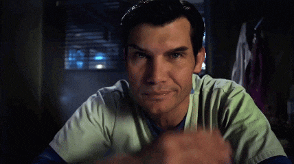 a man in a scrub top looks at the camera with a serious look on his face