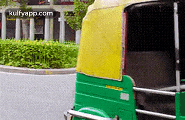 a green and yellow rickshaw is driving down a street in a city .