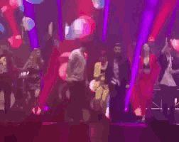 a group of people are dancing on a stage with purple lights
