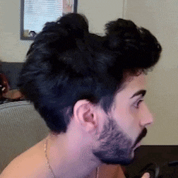 a man with a beard has his hair in a bun and looks surprised