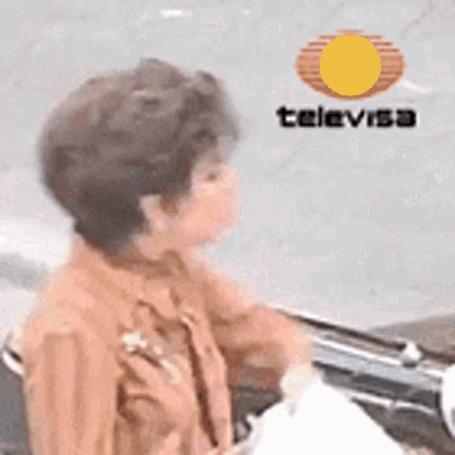 a woman is sitting in front of a televisa logo