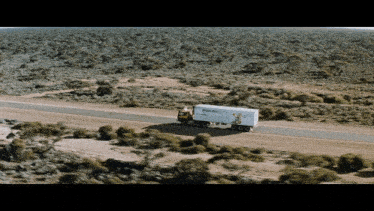 a truck is driving down a dirt road in the desert with a box on the back that says ' moving ' on it