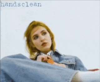 a woman in a denim jacket sits on a white surface with the words handsclean below her