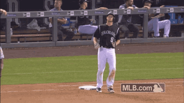 a baseball player wearing a colorado jersey stands on the field