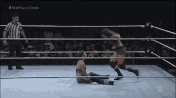 a woman is laying on the ground in a wrestling ring while a referee looks on .