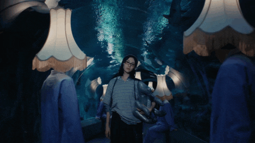 a woman in glasses stands in front of a shark tank