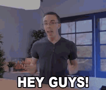 a man with glasses says hey guys in a room