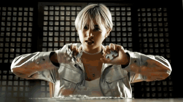 a woman with short blonde hair is sitting at a table with her hands on her chest