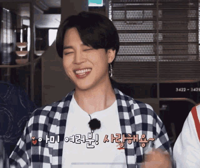 a man wearing a plaid shirt is smiling with a foreign language written on his shirt