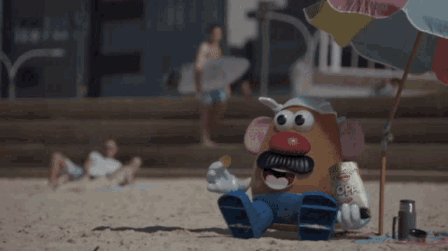 a mr. potato head is sitting on the beach holding a can of dr pepper
