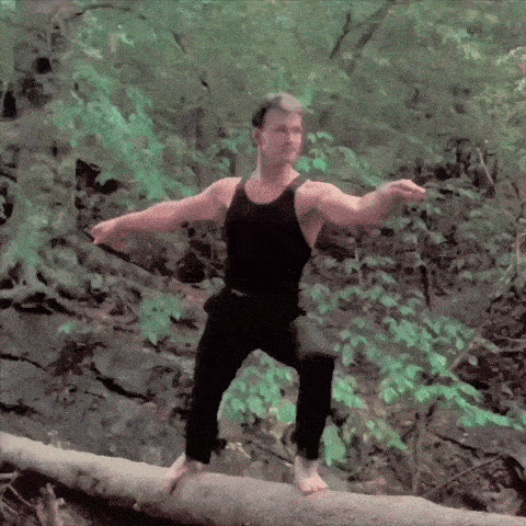 a man in a black tank top balances on a log