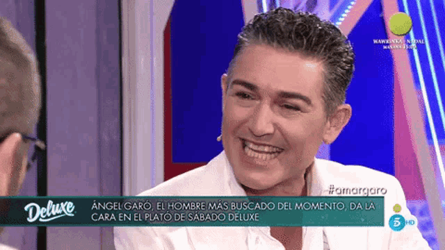 a man in a white shirt is smiling in front of a screen that says deluxe