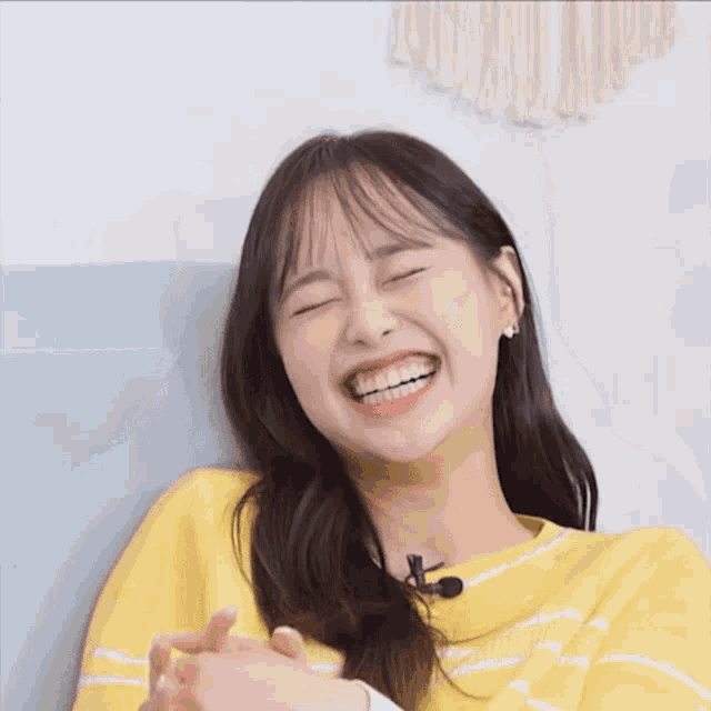 a young woman wearing a yellow sweater and a microphone looks at the camera