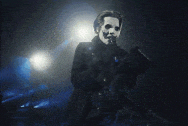 a man with a white face is singing into a microphone in a dark room