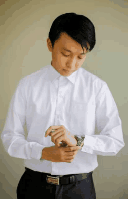 a man in a white shirt and black pants is adjusting his cufflinks while looking at his watch .