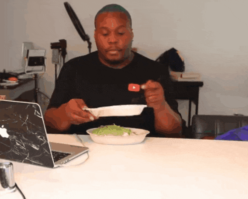 a man sitting at a table with a plate of food in front of a laptop