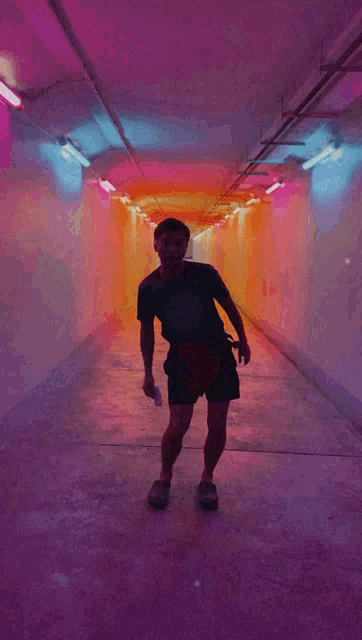 a man in a black shirt is standing in a tunnel with purple and orange lights