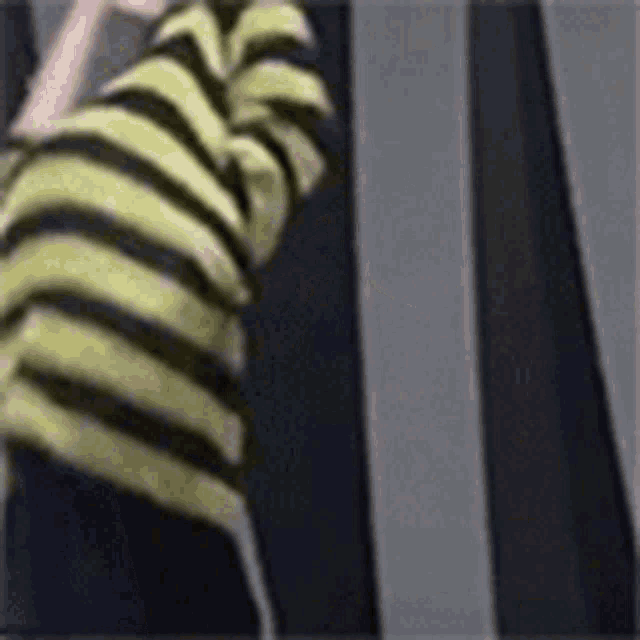 a person wearing a yellow and black striped shirt is standing in front of a black and white striped wall .