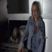 a woman in a denim jacket is standing next to a dead man in a coffin