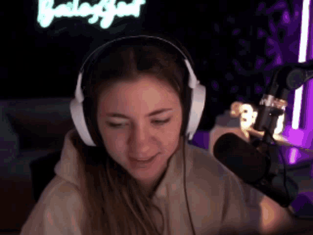 a woman is wearing headphones and a microphone in front of a neon sign .