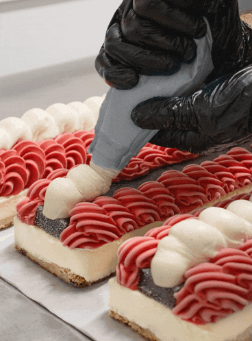 a person wearing black gloves is frosting a cake with red and white frosting