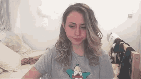 a woman is sitting on a bed wearing a simpson t-shirt .