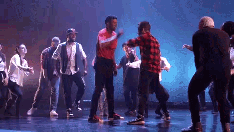 a group of people are dancing on a stage in front of a blue light