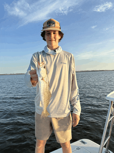 a boy wearing a columbia shirt holds a small fish