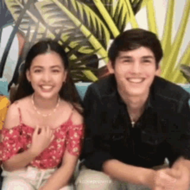 a boy and a girl are sitting next to each other on a couch and smiling .