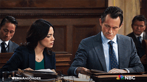 a man and a woman sitting in a courtroom with a nbc logo on the bottom