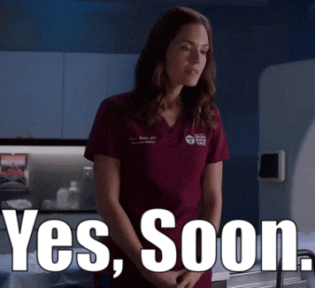 a woman in a scrub top is standing in front of a sign that says yes soon