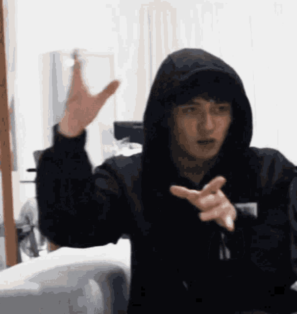 a young man wearing a black hoodie is making a funny face while sitting on a couch .