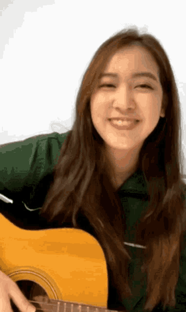 a woman is playing an acoustic guitar and smiling .