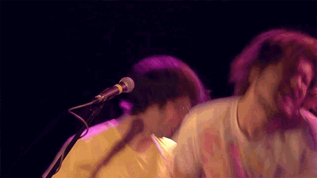 a man is singing into a microphone while another man looks on