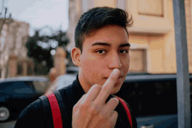 a young man with a red backpack is giving the middle finger to the camera