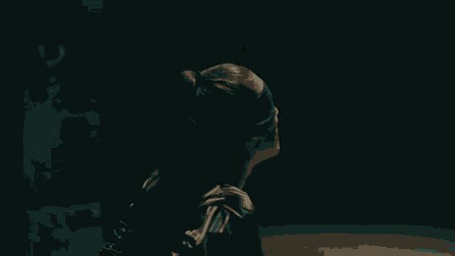 a man in a black jacket is standing in a dark hallway looking at the camera .