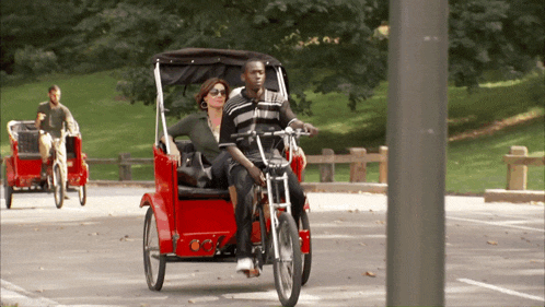 a man and a woman are riding a red rickshaw in a park