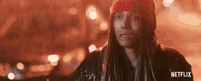 a woman in a red hat is crying in the rain with a netflix logo in the corner .