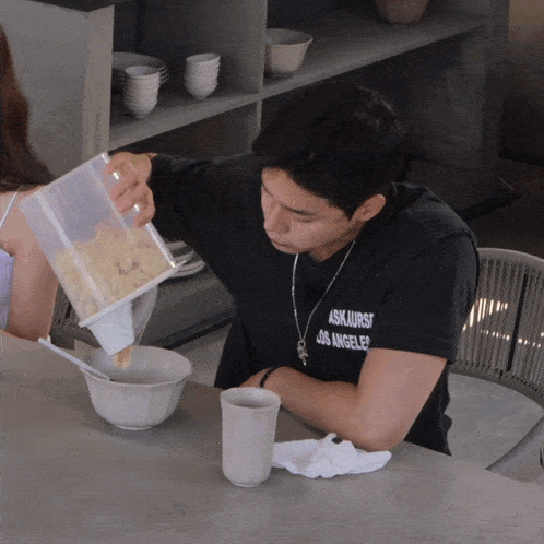 a man is pouring cereal into a bowl while wearing a black shirt that says askjurs los angeles