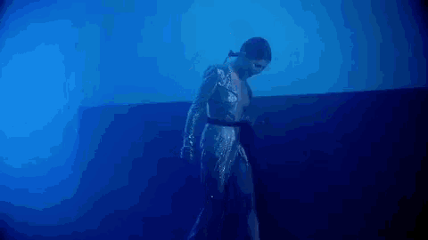 a woman in a sequined dress is dancing in a dark room in a blue light .