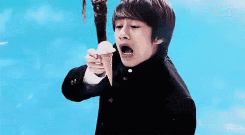 a young boy in a school uniform is holding an ice cream cone with his mouth open .