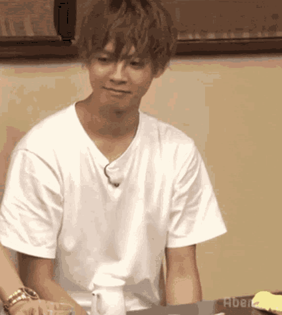 a young man wearing a white t-shirt is sitting at a table with a cup of coffee .