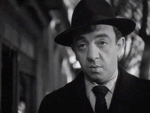 a man wearing a hat and tie is looking at the camera