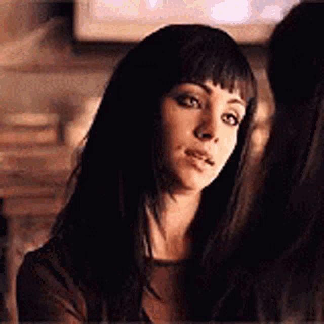 a woman with long black hair and bangs is looking at another woman 's face .