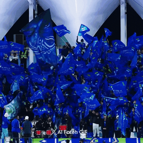 a crowd of people are waving blue flags that say al fateh